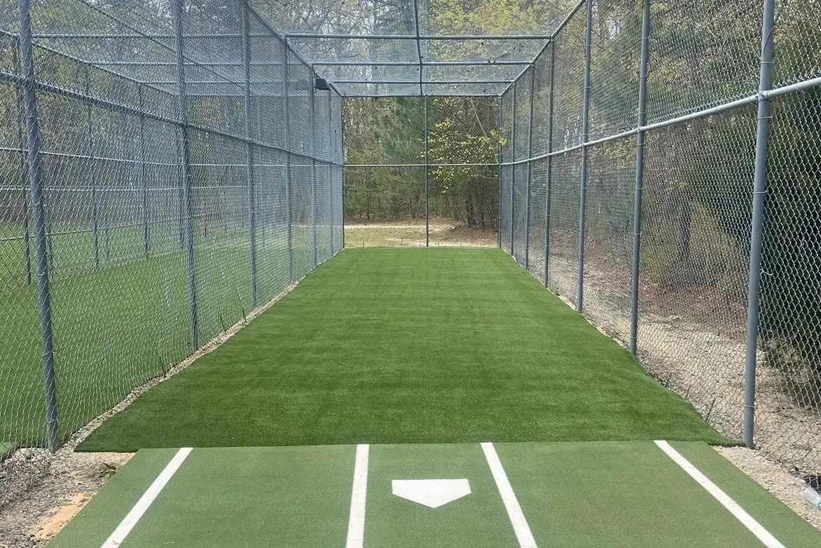 A baseball field with a batting cage and green grass.