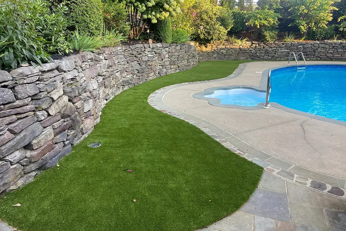 A pool with a stone wall and grass