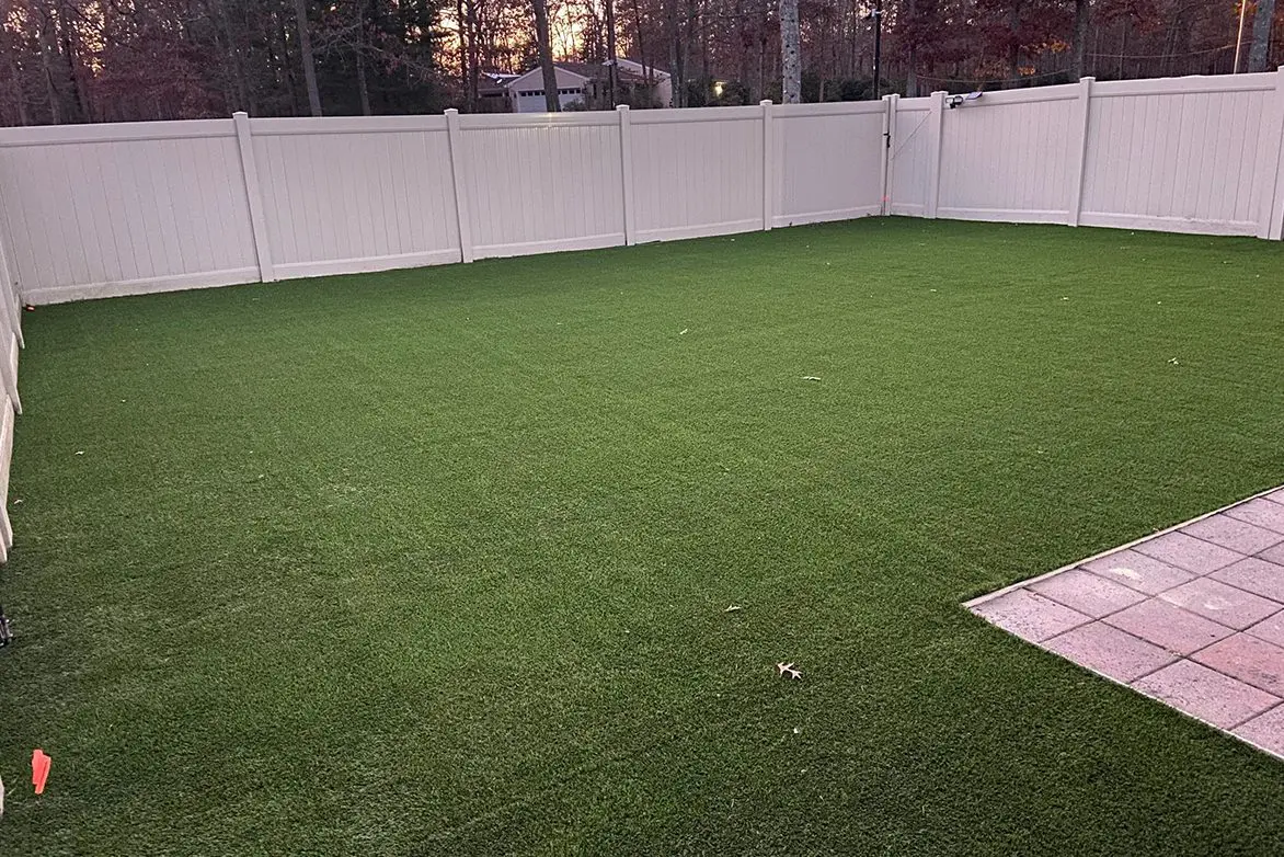 A backyard with a white fence and grass.