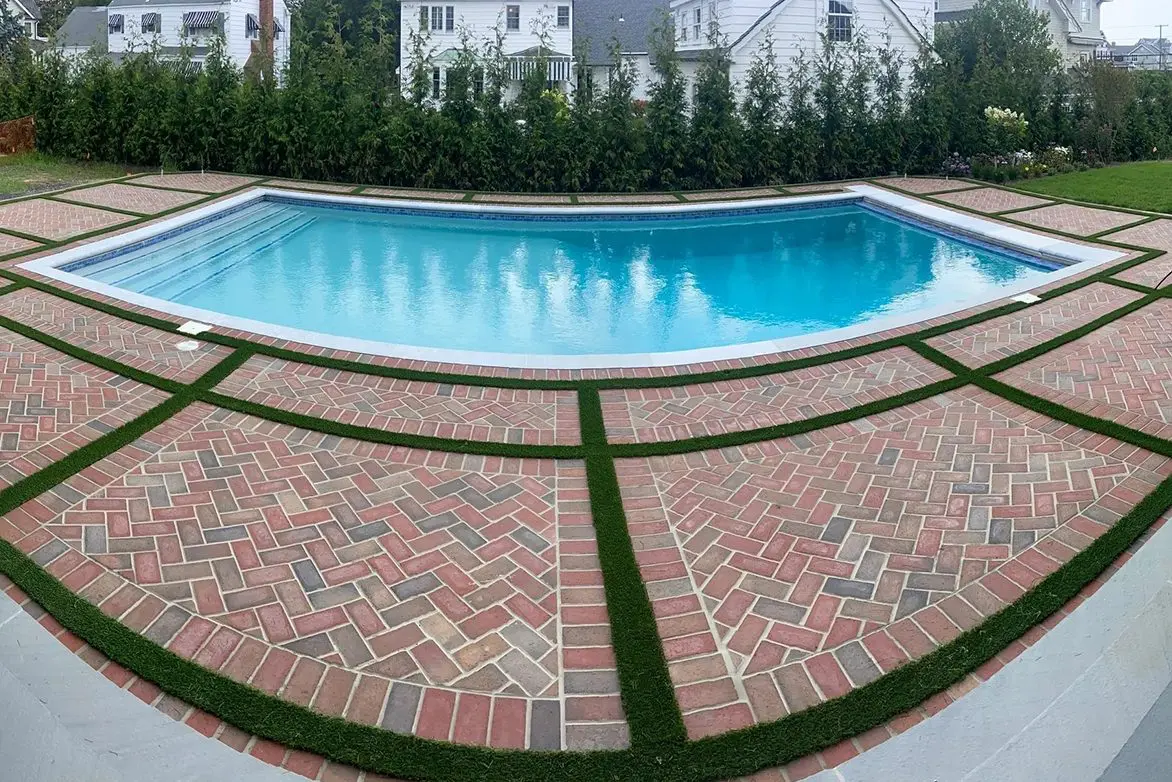 A pool with brick pavers and grass around it.